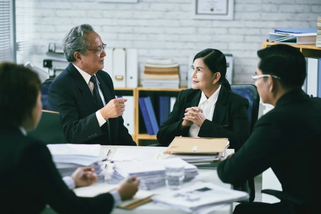 Group of business professionals in formal attire discussing documents in an office, representing legal consultation for setting up a business in Dubai.