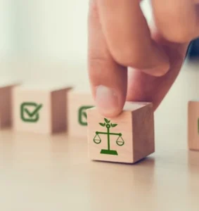 Hand picking a wooden block with a green scale of justice icon, symbolizing legal responsibility and accountability in UAE product liability cases.