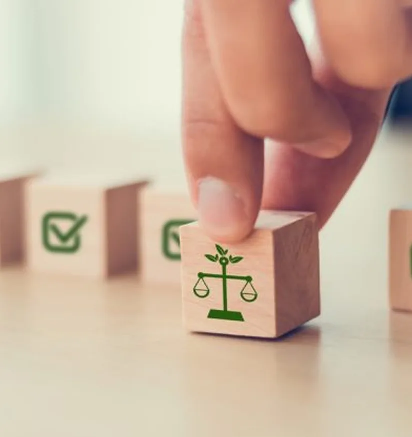 Hand picking a wooden block with a green scale of justice icon, symbolizing legal responsibility and accountability in UAE product liability cases.
