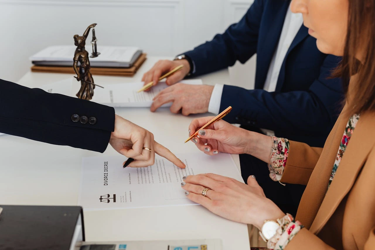 Lawyer pointing to a section of a legal document while a couple reviews and prepares to sign, symbolizing legal consultation for a prenuptial or divorce agreement.