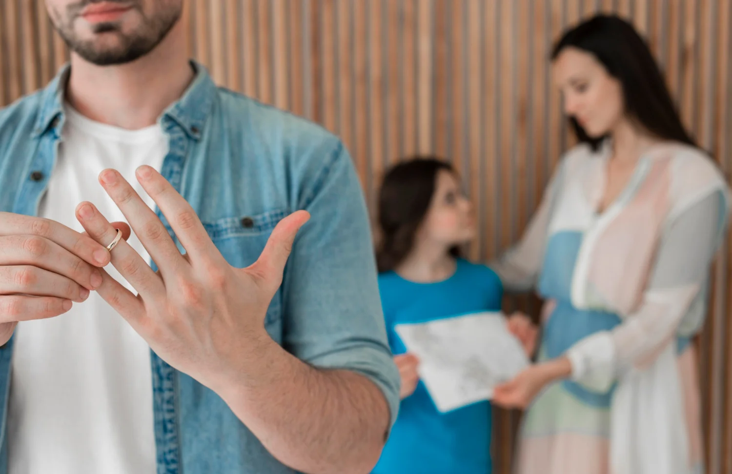 A man is taking off the wedding ring while a woman and a young girl hold a piece of paper in the back.