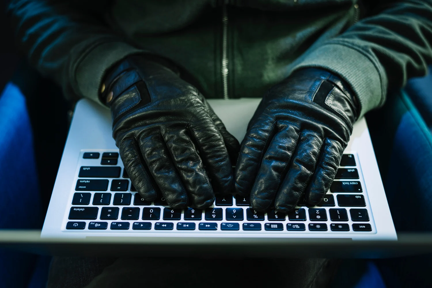A hacker with black gloves typing keys on a laptop