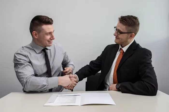 Two men shaking hands with a contract in front of them