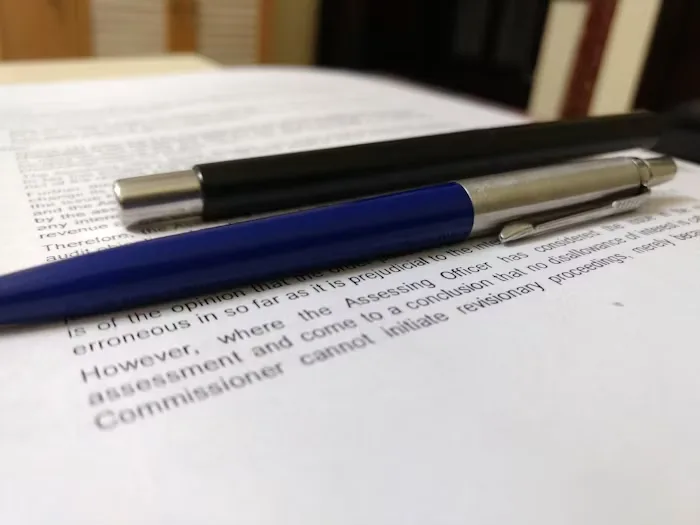 A legal agreement with two pens on the papers, one black and one blue 